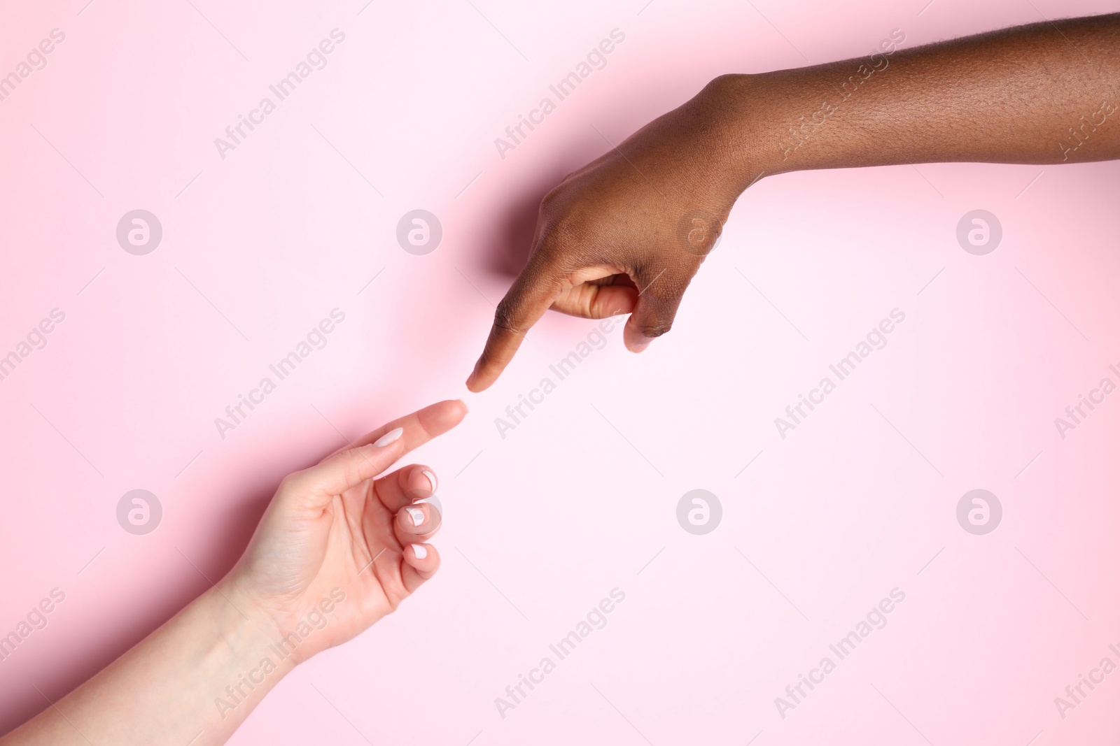 Photo of Stop racism. People of different skin colors joining hands on light pink background, closeup