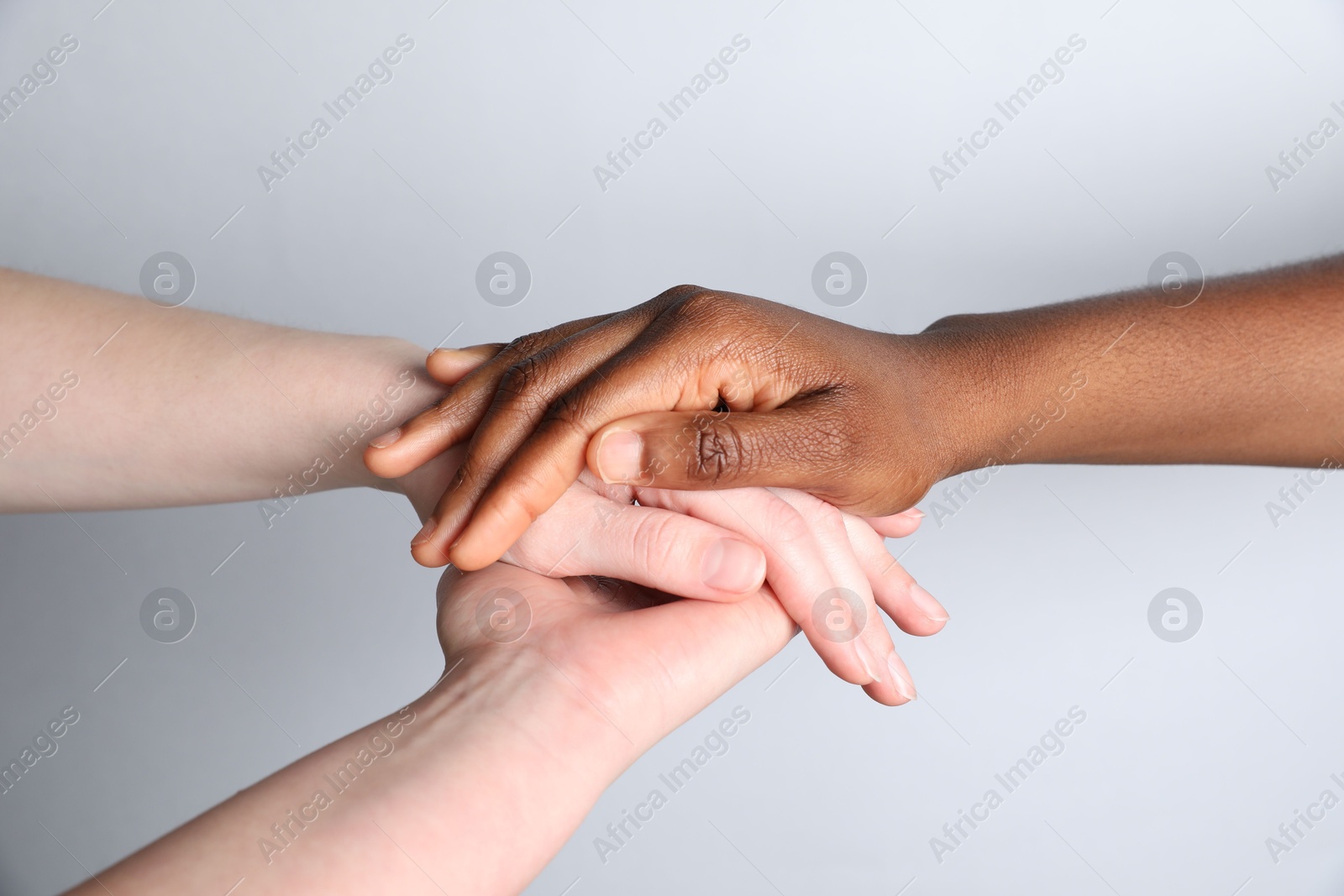 Photo of Stop racism. People of different skin colors holding hands on light grey background, closeup