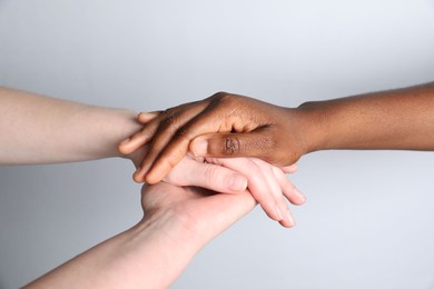 Photo of Stop racism. People of different skin colors holding hands on light grey background, closeup