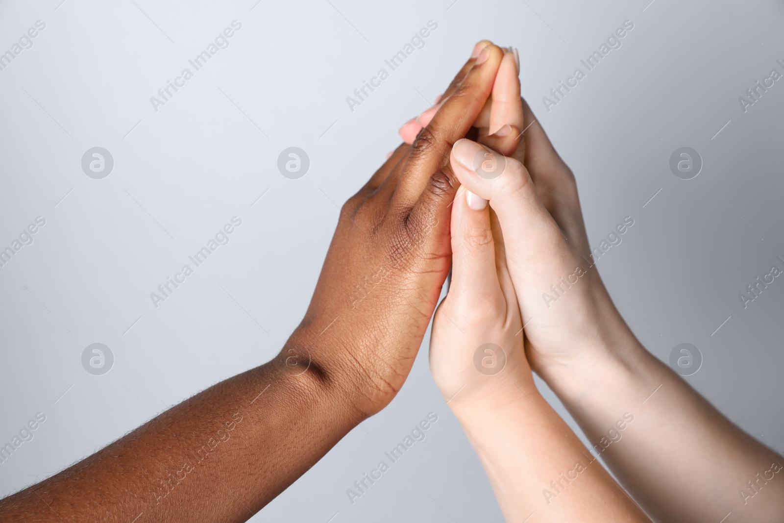 Photo of Stop racism. People of different skin colors joining hands on light grey background, closeup