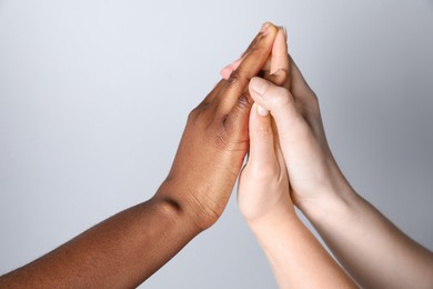 Photo of Stop racism. People of different skin colors joining hands on light grey background, closeup