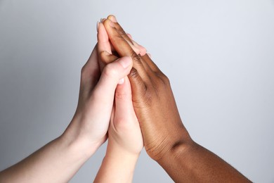 Photo of Stop racism. People of different skin colors joining hands on light grey background, closeup