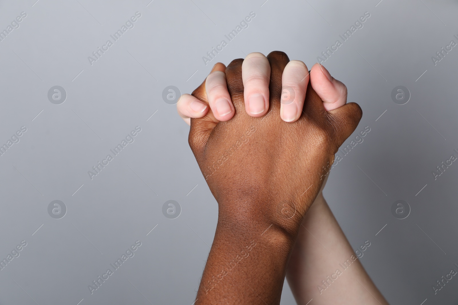 Photo of Stop racism. People of different skin colors holding hands on light grey background, closeup