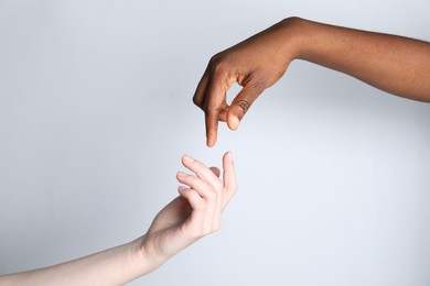 Photo of Stop racism. People of different skin colors joining hands on light grey background, closeup