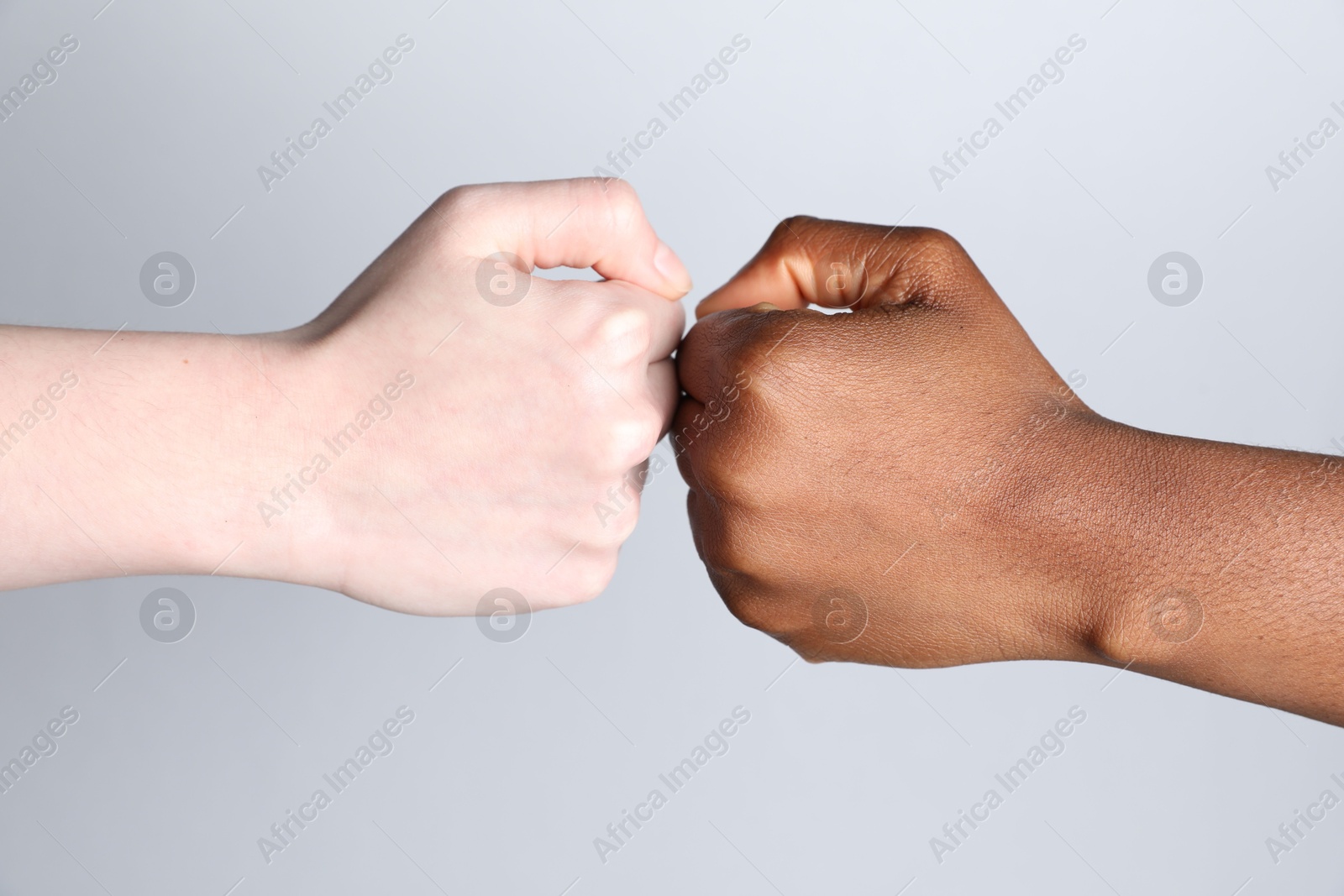 Photo of Stop racism. People of different skin colors bumping fists on light grey background, closeup