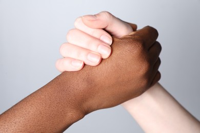 Photo of Stop racism. People of different skin colors holding hands on light grey background, closeup