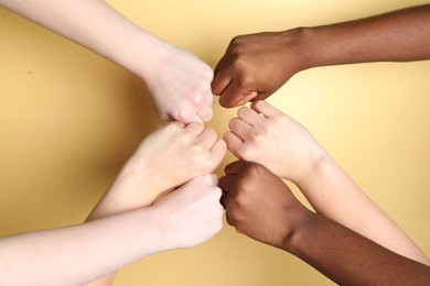 Photo of Stop racism. People of different skin colors bumping fists on beige background, closeup