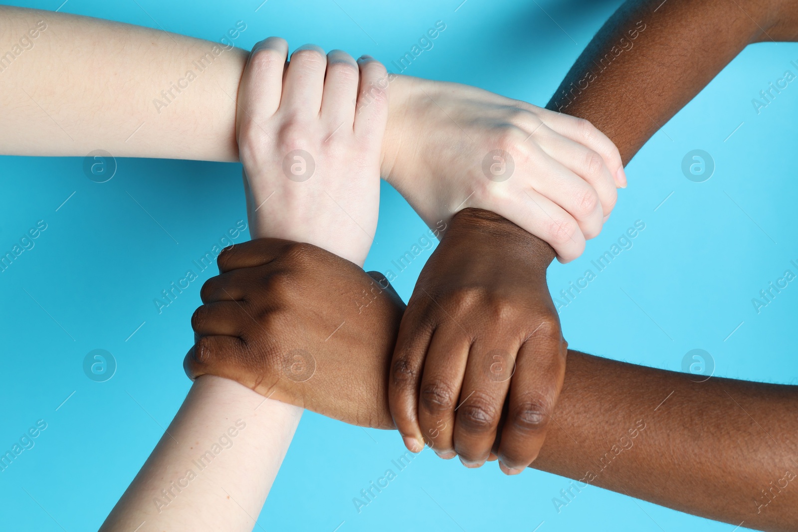 Photo of Stop racism. People of different skin colors joining hands on light blue background, closeup