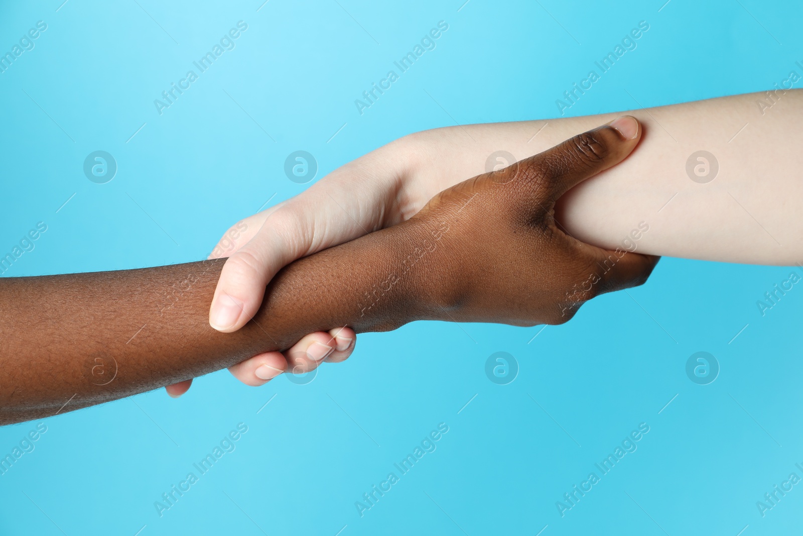 Photo of Stop racism. People of different skin colors holding hands on light blue background, closeup