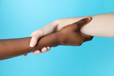 Photo of Stop racism. People of different skin colors holding hands on light blue background, closeup