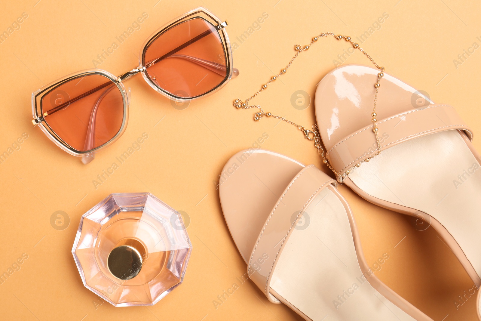 Photo of Shoes, perfume and stylish accessories on pale orange background, flat lay