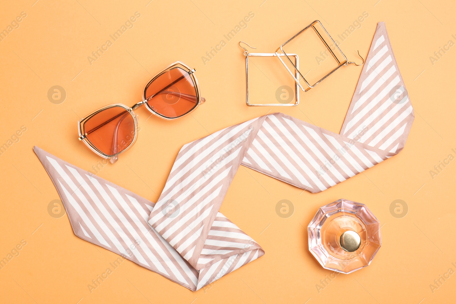 Photo of Perfume and stylish accessories on pale orange background, flat lay