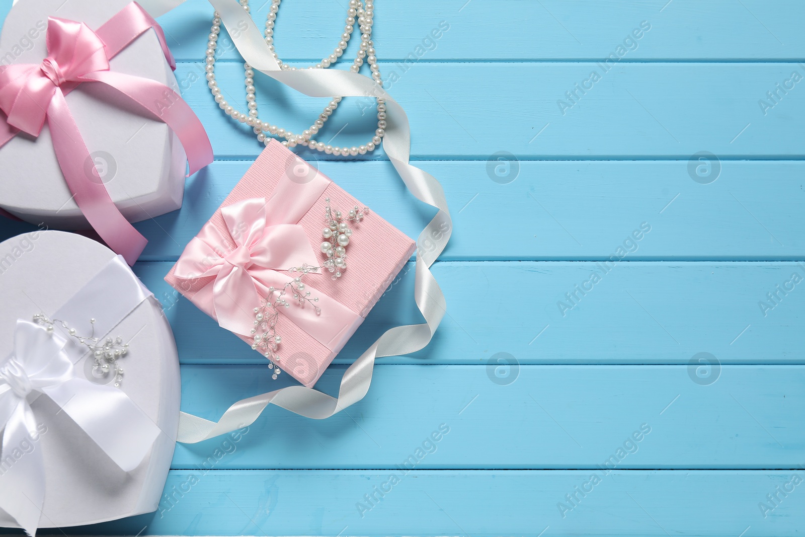 Photo of Beautiful wedding gifts, ribbon and pearl jewelry on light blue wooden table, flat lay. Space for text