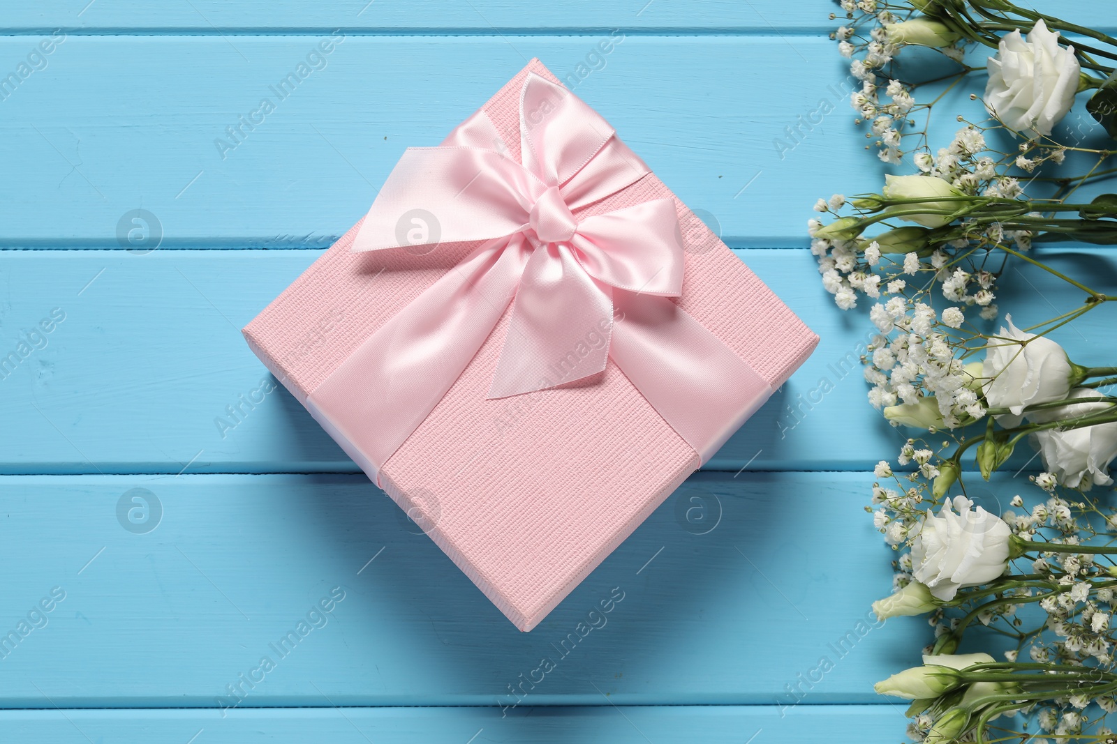 Photo of Beautiful wedding gift and flowers on light blue wooden table, flat lay