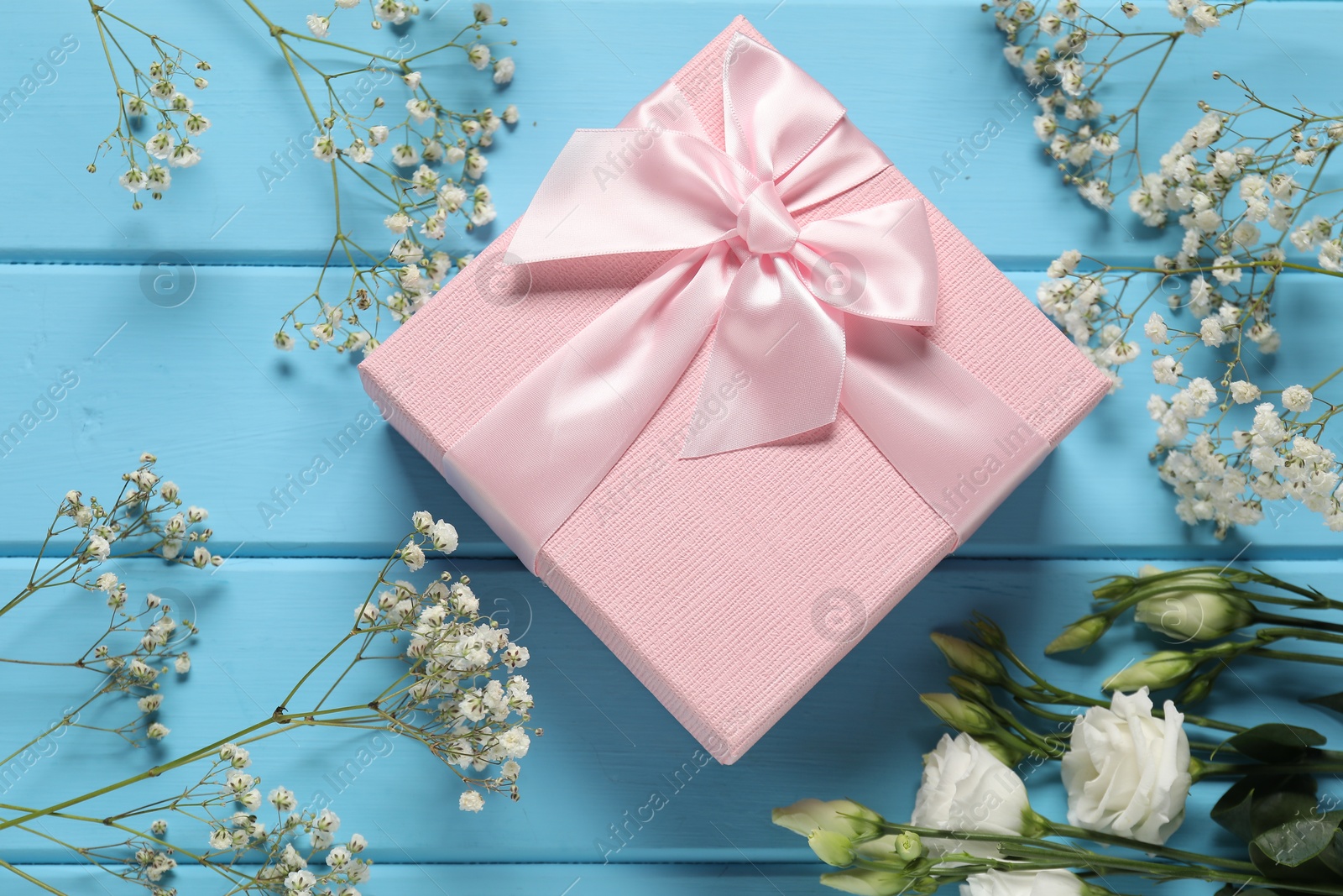 Photo of Beautiful wedding gift and flowers on light blue wooden table, flat lay