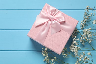 Photo of Beautiful wedding gift and gypsophila flowers on light blue wooden table, flat lay. Space for text