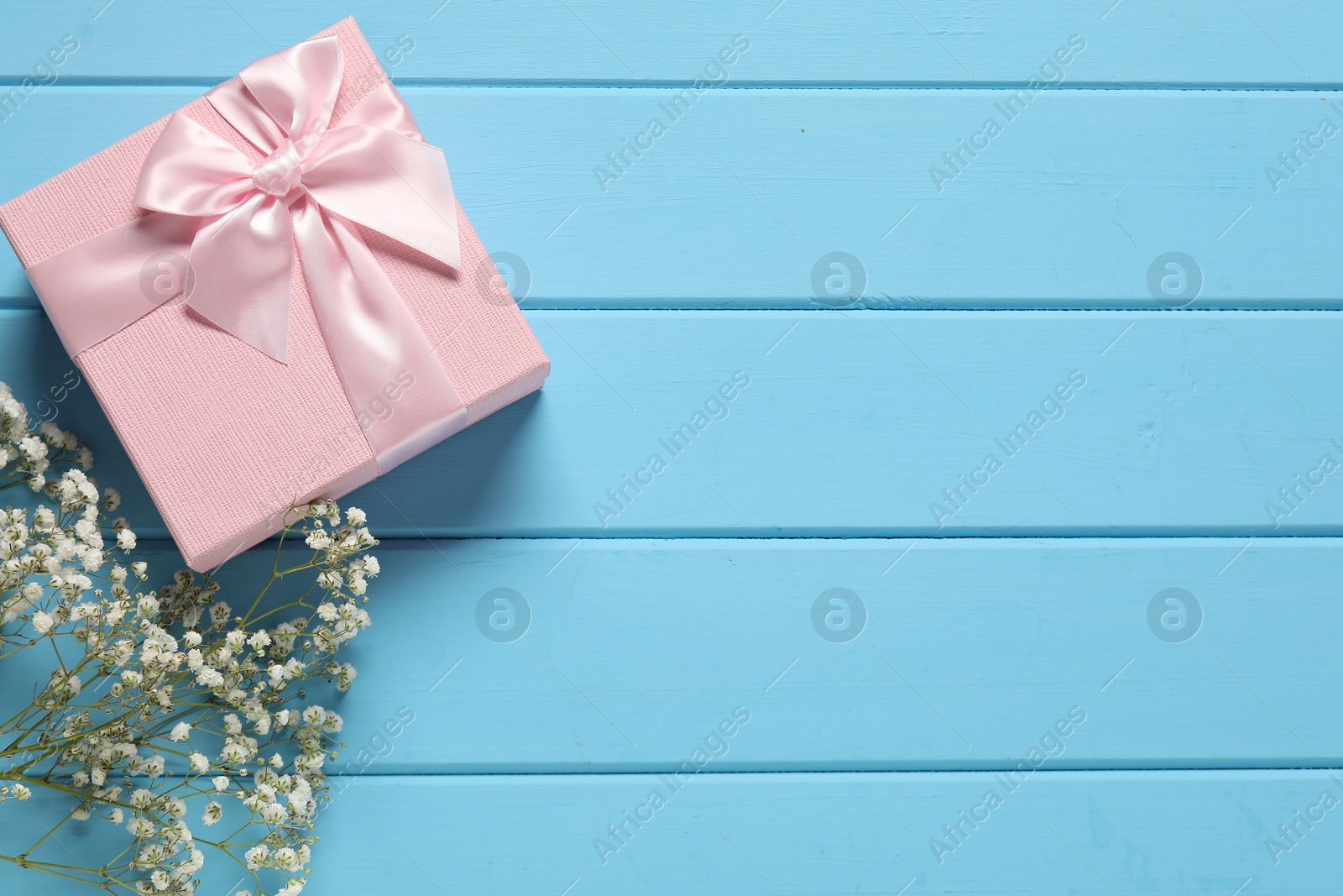 Photo of Beautiful wedding gift and gypsophila flowers on light blue wooden table, flat lay. Space for text