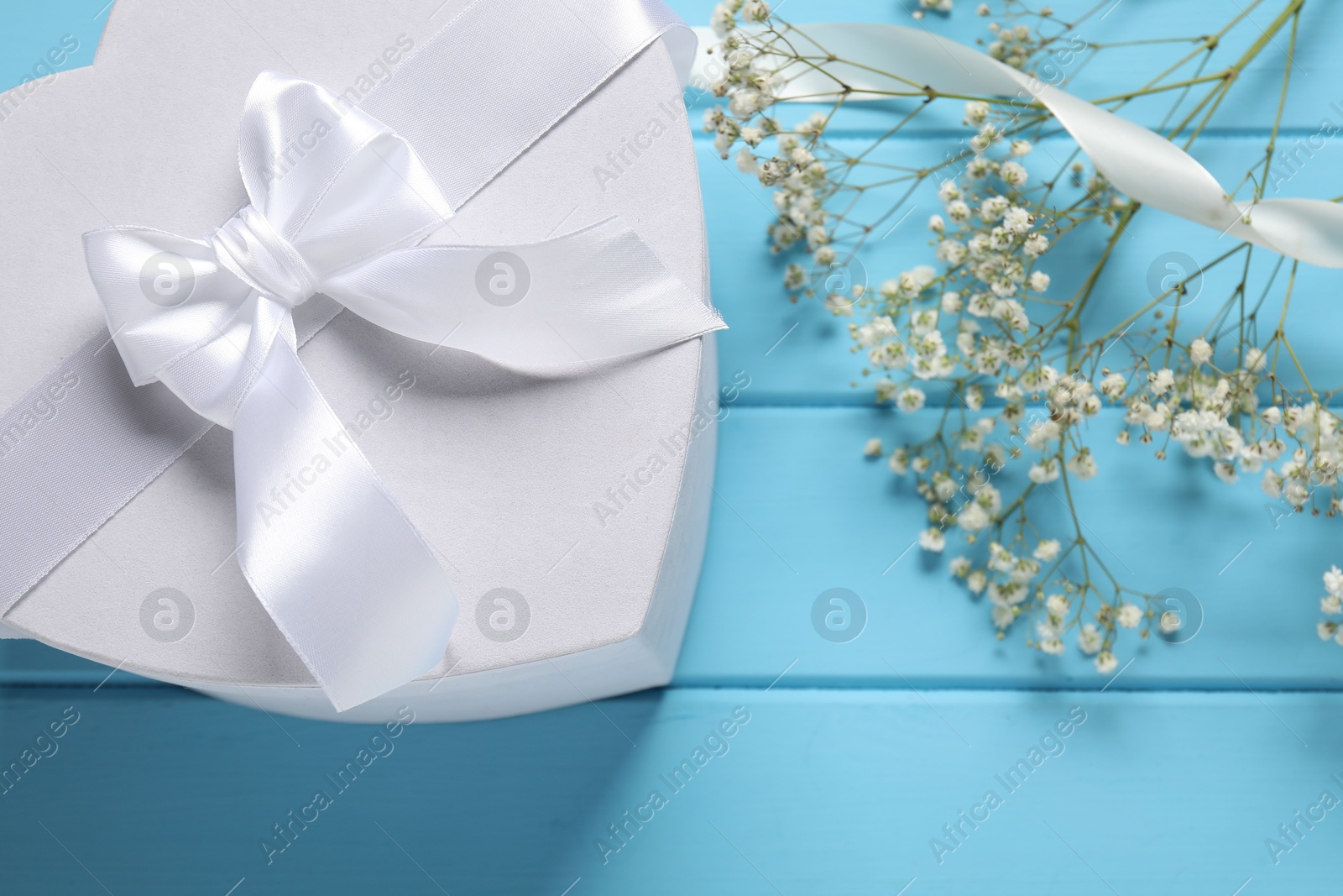 Photo of Beautiful wedding gift, ribbon and gypsophila flowers on light blue wooden table, flat lay