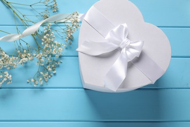 Photo of Beautiful wedding gift, ribbon and gypsophila flowers on light blue wooden table, flat lay