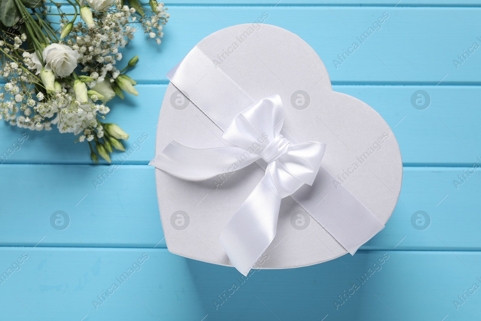 Photo of Beautiful wedding gift and flowers on light blue wooden table, flat lay