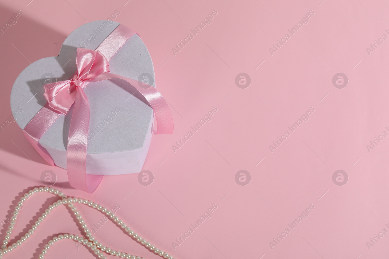 Photo of Beautiful wedding gift and pearl jewelry on pink background, flat lay. Space for text