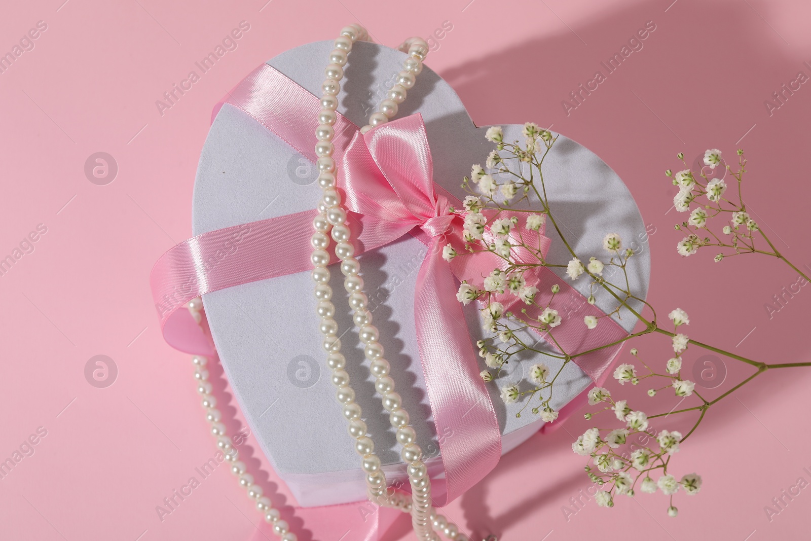 Photo of Beautiful wedding gift, pearl jewelry and gypsophila flowers on pink background, flat lay