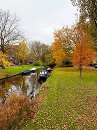 Photo of Beautiful view of canal with moored boats and colorful fallen leaves on autumn day