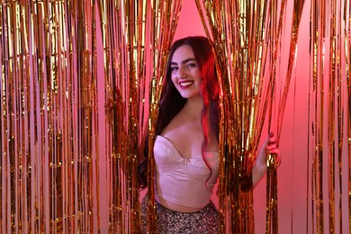 Photo of Happy young woman looking out through golden foil curtain in neon lights