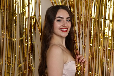 Photo of Portrait of beautiful young woman near golden foil curtain against beige background