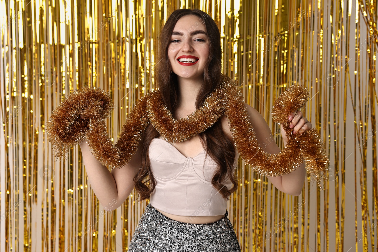 Photo of Happy young woman with tinsel against golden foil curtain