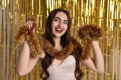 Photo of Happy young woman with tinsel against golden foil curtain