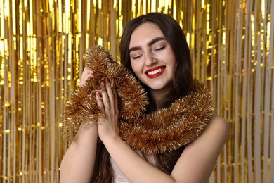 Photo of Happy young woman with tinsel against golden foil curtain