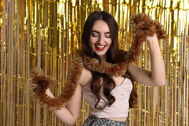 Photo of Happy young woman with tinsel against golden foil curtain