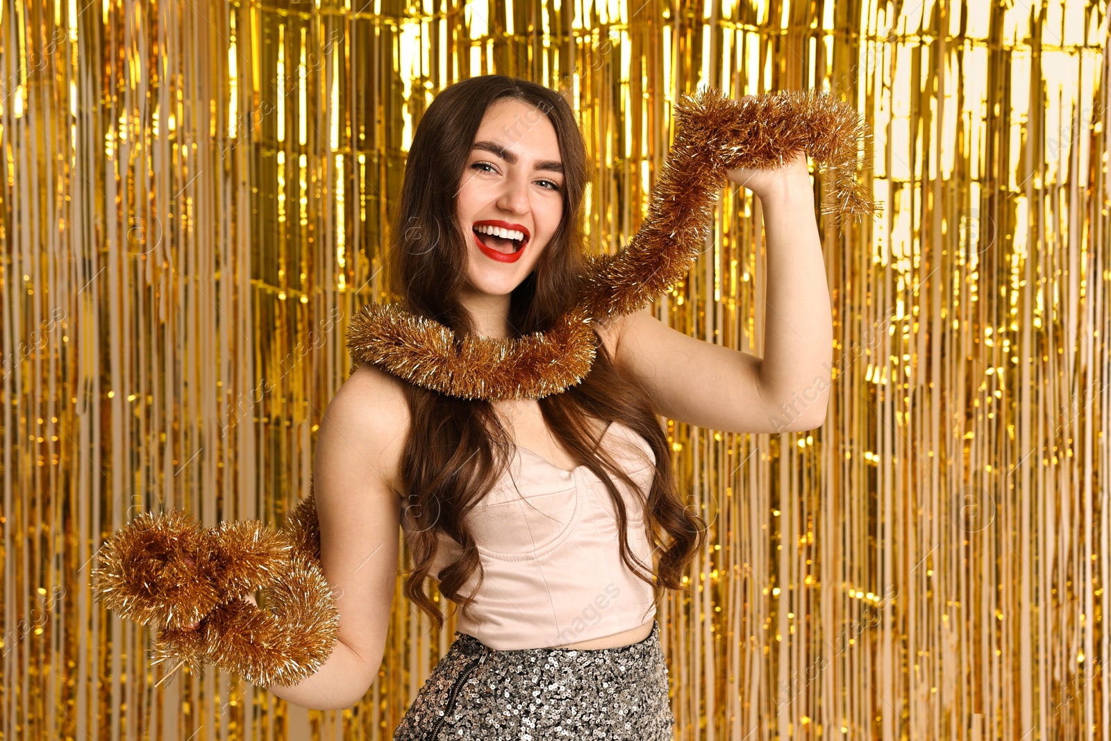 Photo of Happy young woman with tinsel against golden foil curtain