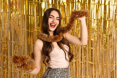 Photo of Happy young woman with tinsel against golden foil curtain