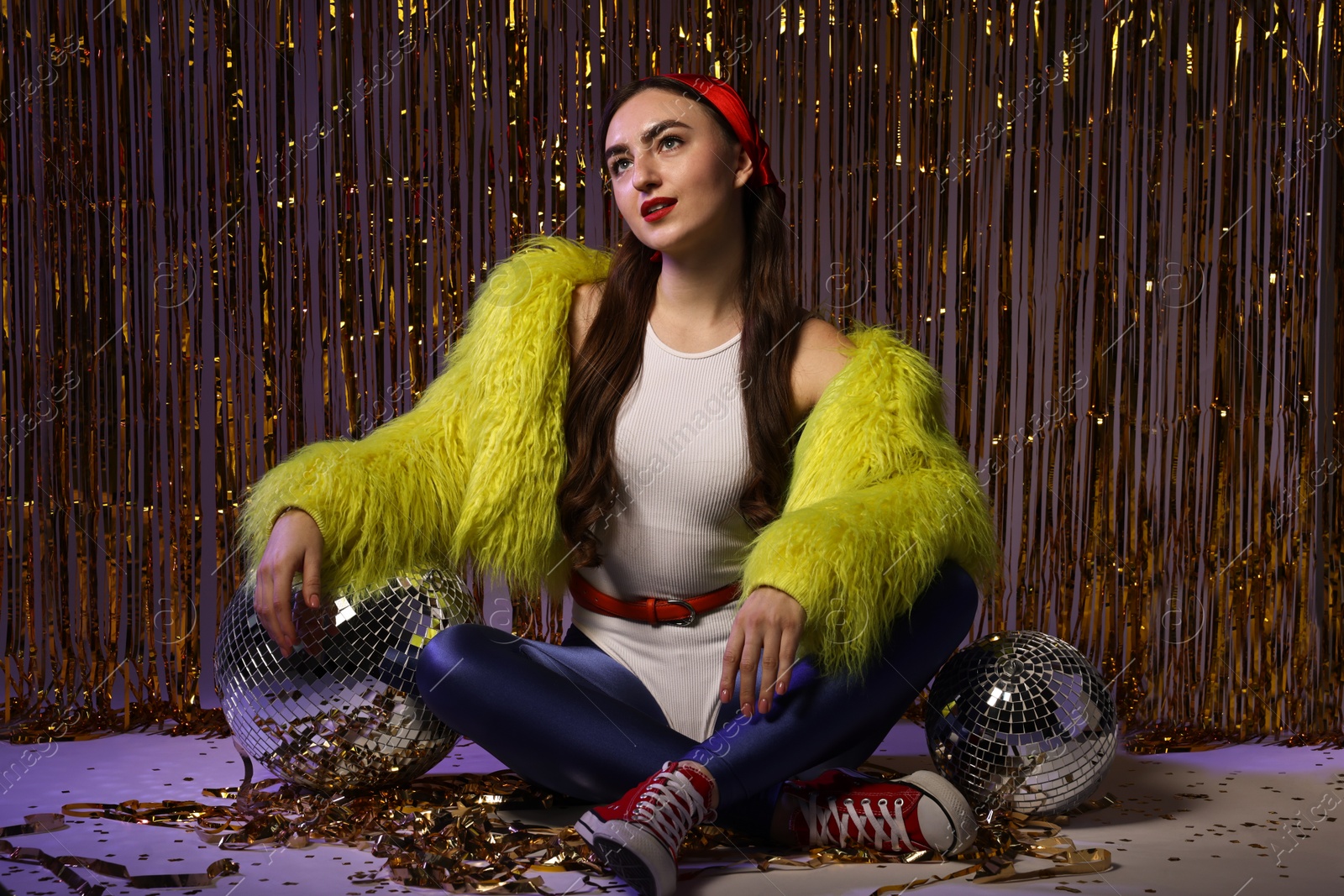 Photo of Beautiful young woman in retro outfit with shiny tinsel and disco balls indoors