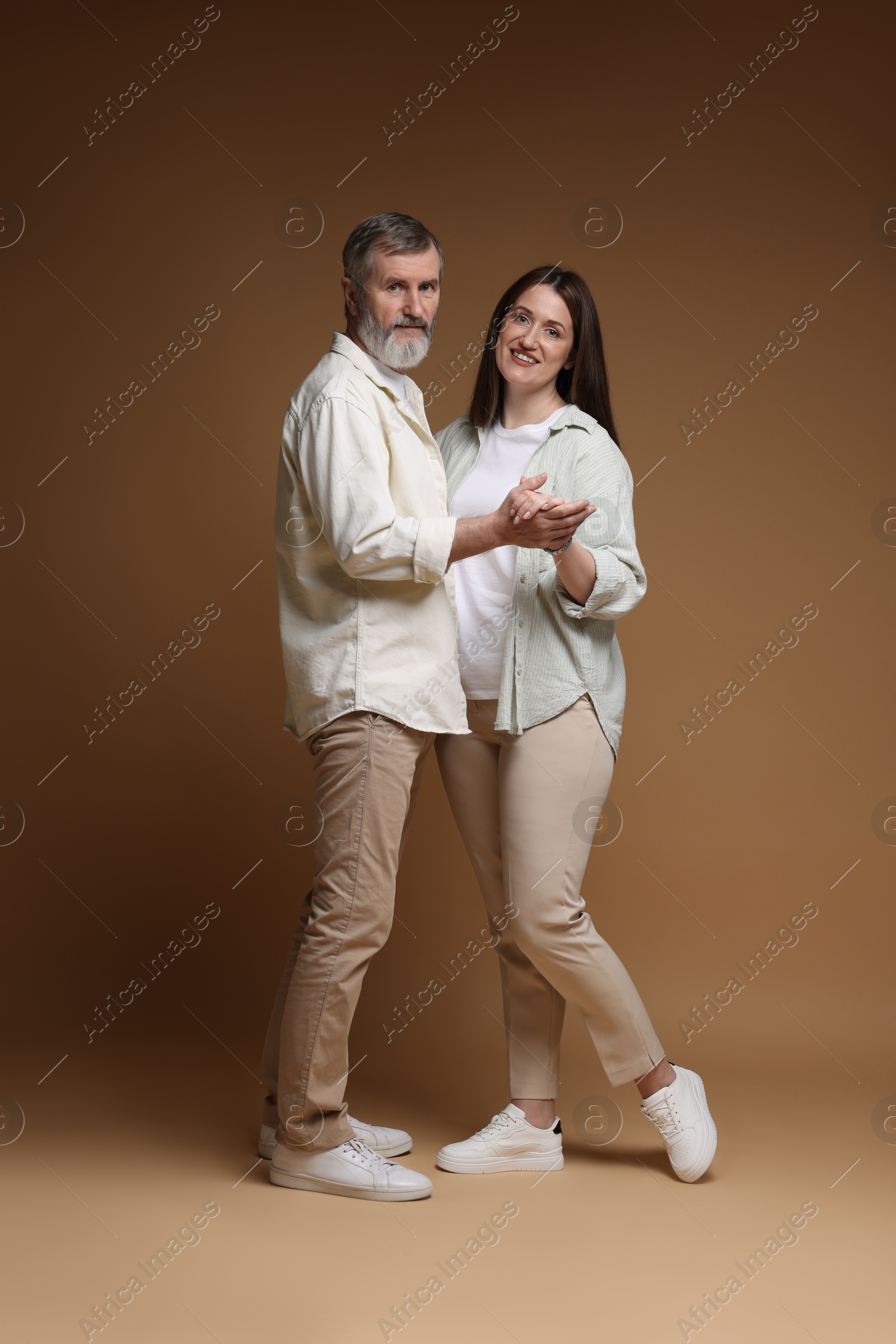 Photo of Happy daughter dancing with her father on brown background