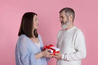 Photo of Happy daughter presenting her father with gift on pink background