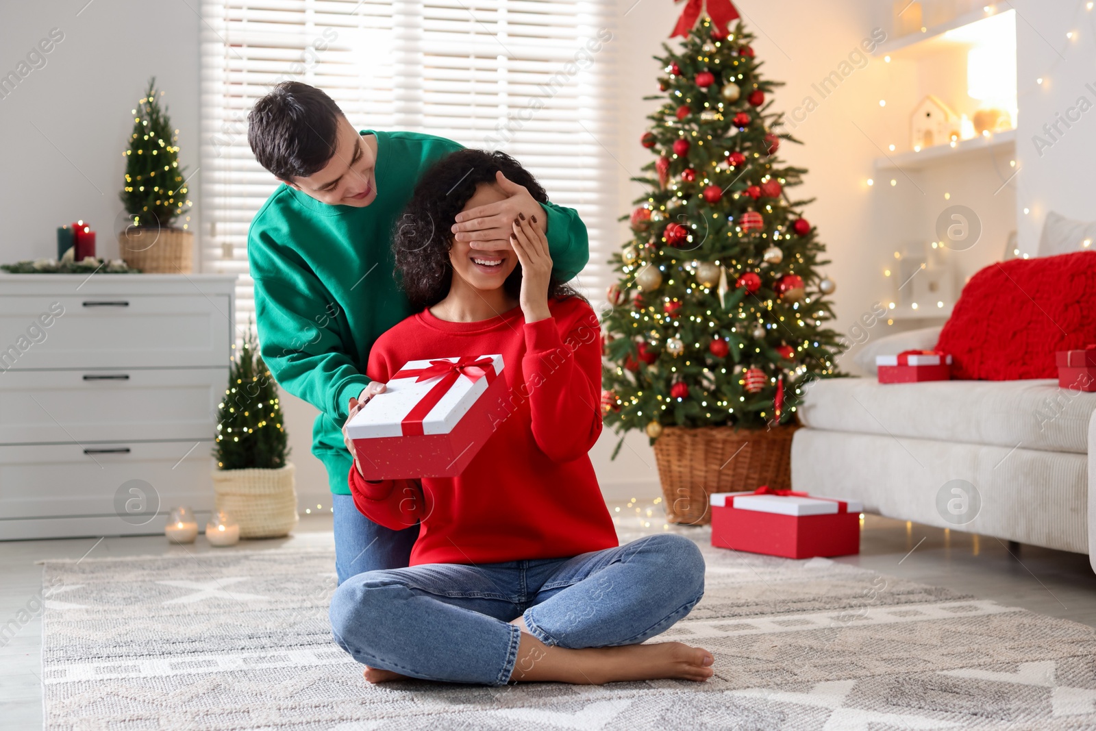 Photo of Happy man surprising his girlfriend with Christmas gift at home