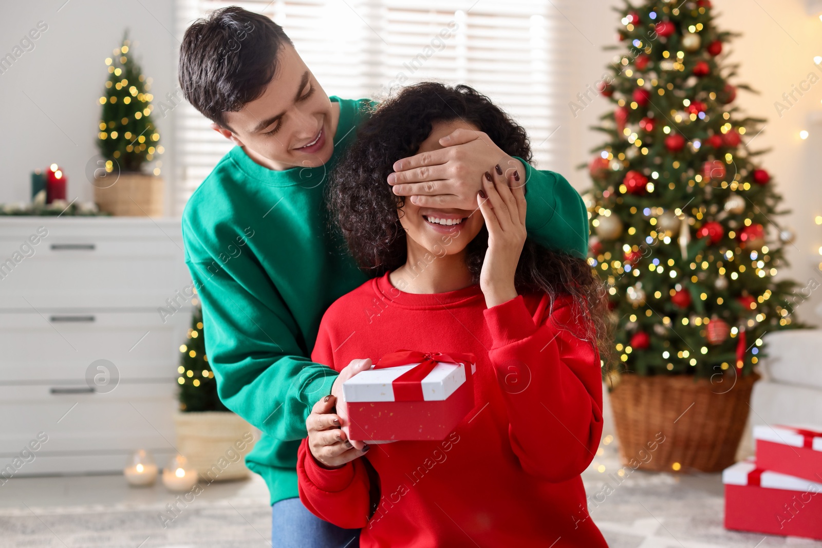 Photo of Happy man surprising his girlfriend with Christmas gift at home