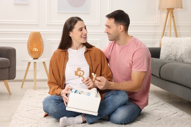 Photo of Pregnant woman and her husband with box of baby toys and booties at home