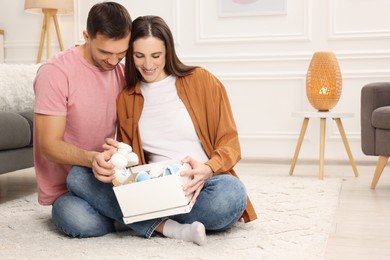 Photo of Pregnant woman and her husband with box of baby toys and booties at home. Space for text