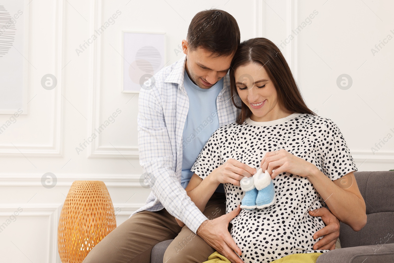 Photo of Pregnant woman and her husband with baby booties at home. Space for text