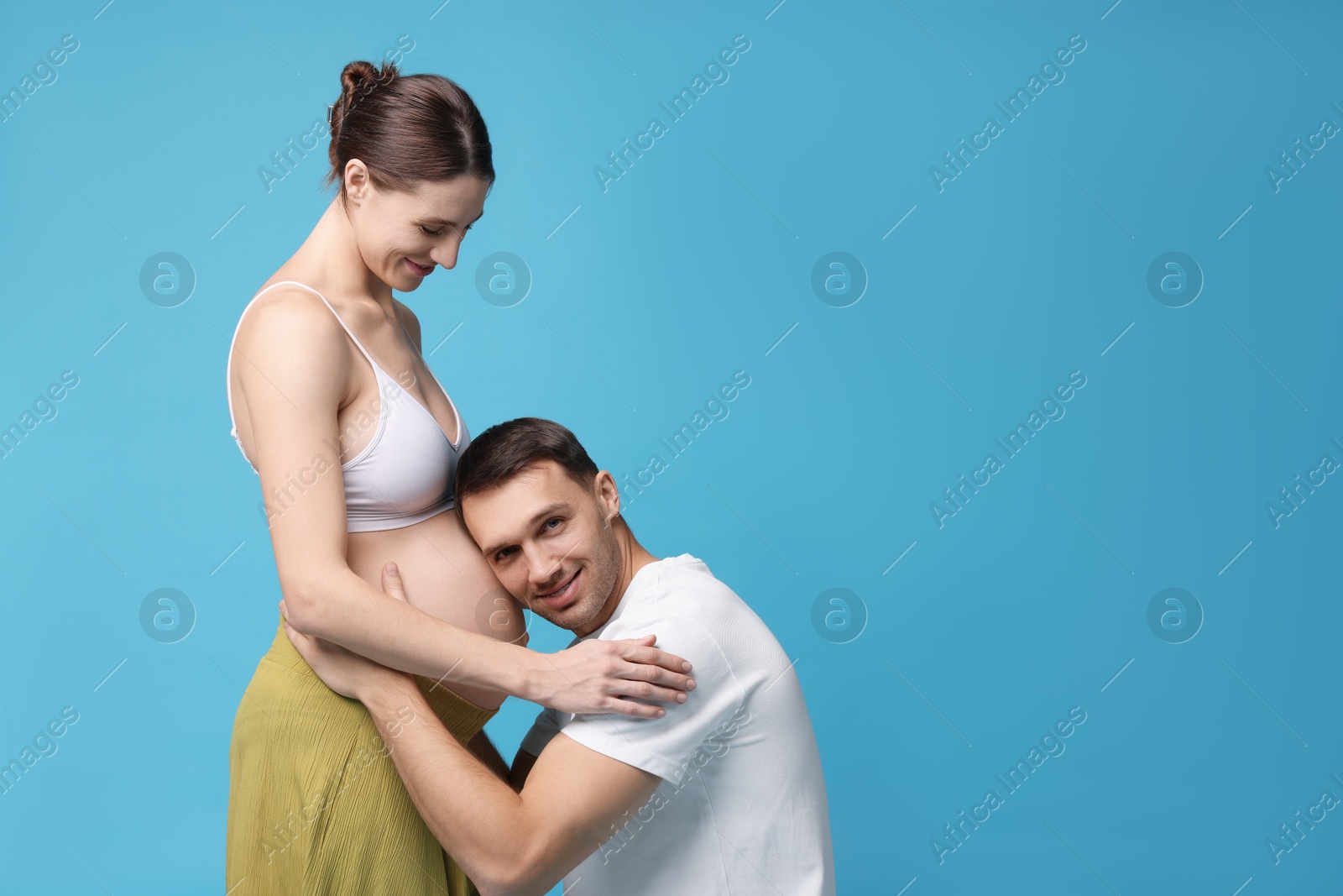 Photo of Man listening to baby in his pregnant wife's belly on blue background. Space for text