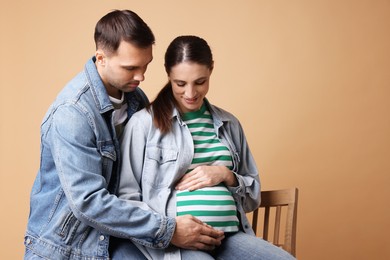 Photo of Man trying to feel baby kicks in his pregnant wife's belly on beige background