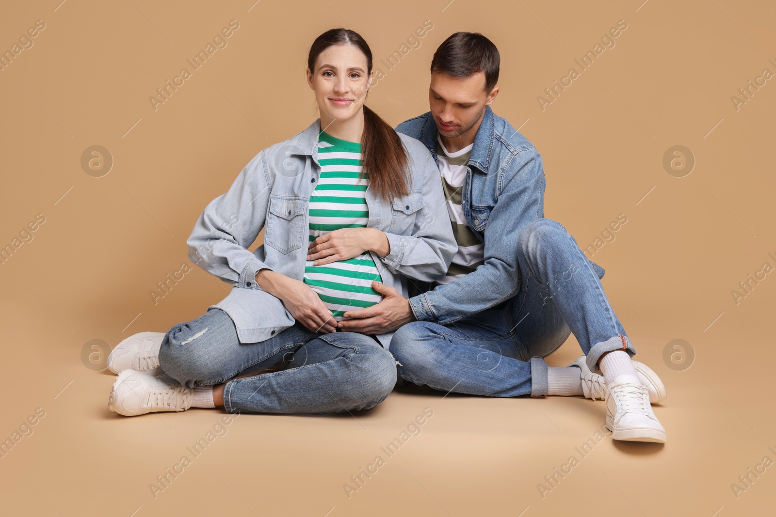 Photo of Pregnant woman and her husband on beige background