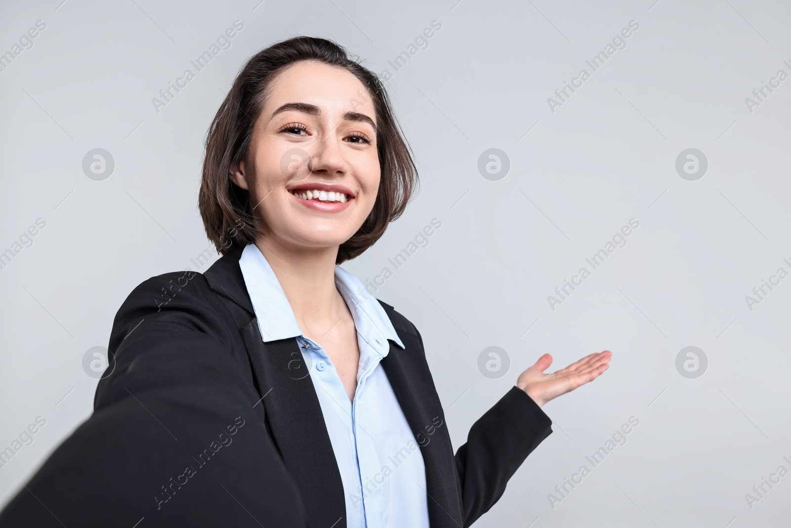 Photo of Happy businesswoman welcoming clients or partners via video call on light grey background