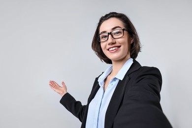 Photo of Happy businesswoman welcoming clients or partners via video call on light grey background