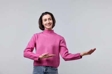 Photo of Cheerful woman welcoming friends or guests on light grey background