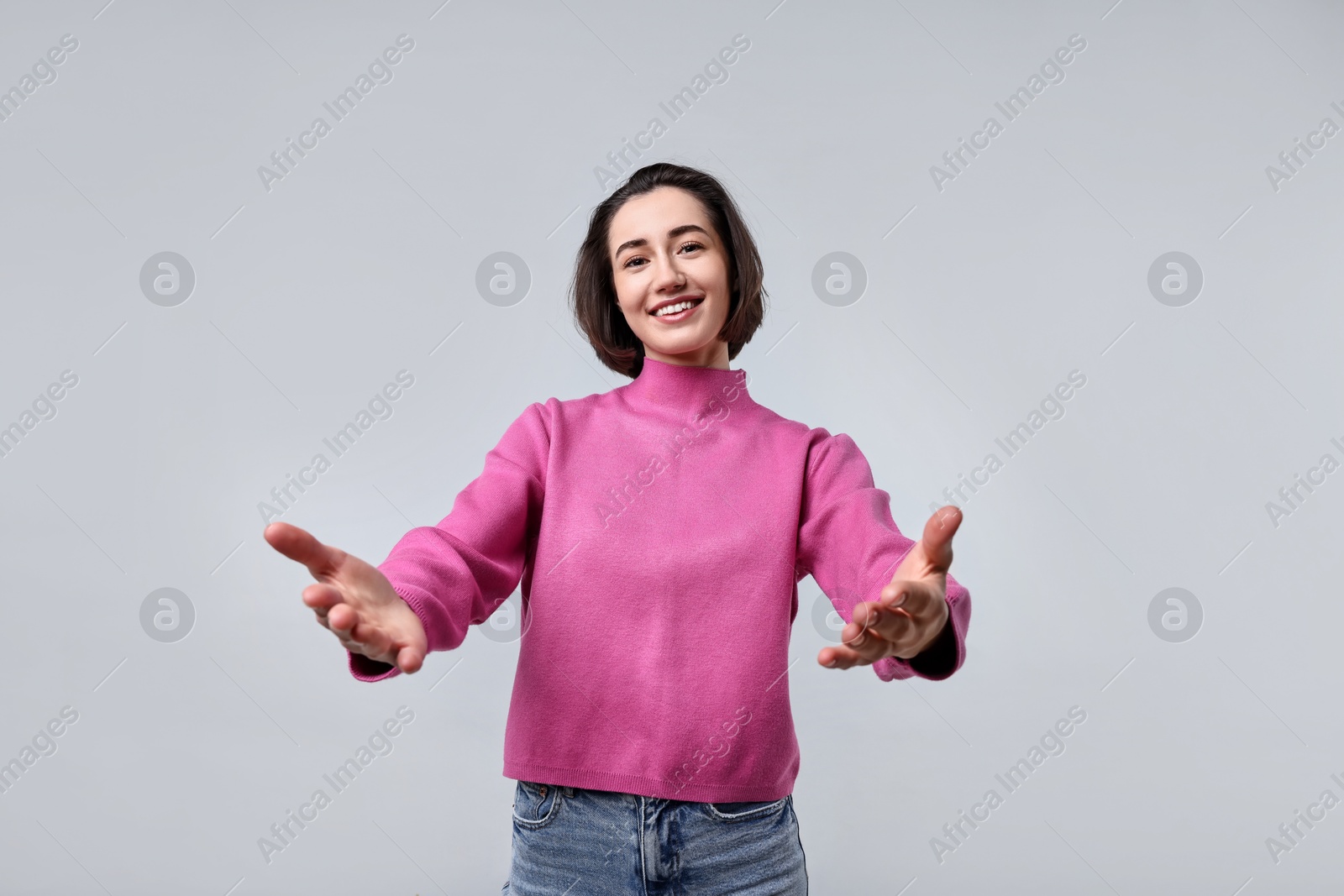 Photo of Cheerful woman welcoming friends or guests on light grey background